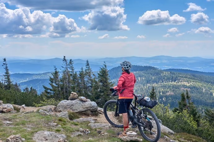 woman on a bike packing tour with her electric mountain bike in the rocky the summit of Great Arber in the Bavarian Forest, Bavaria, Germany
