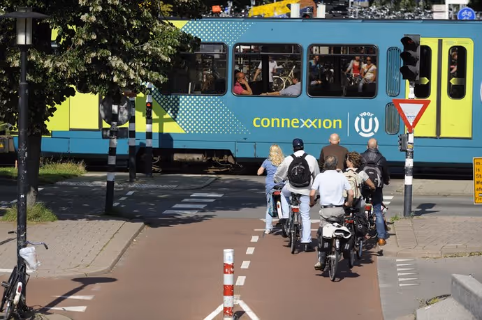 Small group of cyclists waiting at red traffic light in Utrecht. A tram is passing by. Location: Smakkelaarsveld, adjacent to the bus station and Utrecht central railway statio