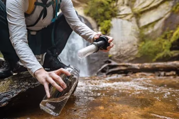 A man gathering water from a stream using a Camelbak Eddy with built-in LifeStraw filter.