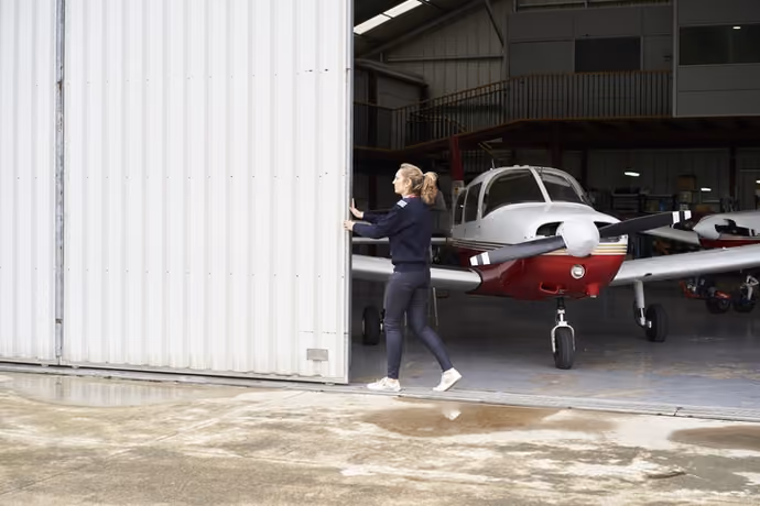pilot opening the door of the hangar where there are several small aircraft stored.