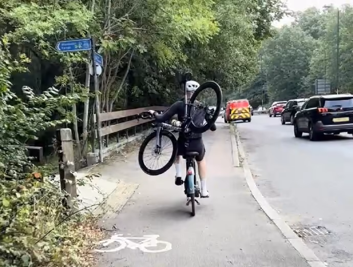 a rider wobbling through town on a Lime hire bike, their own punctured machine awkwardly balanced across their shoulders