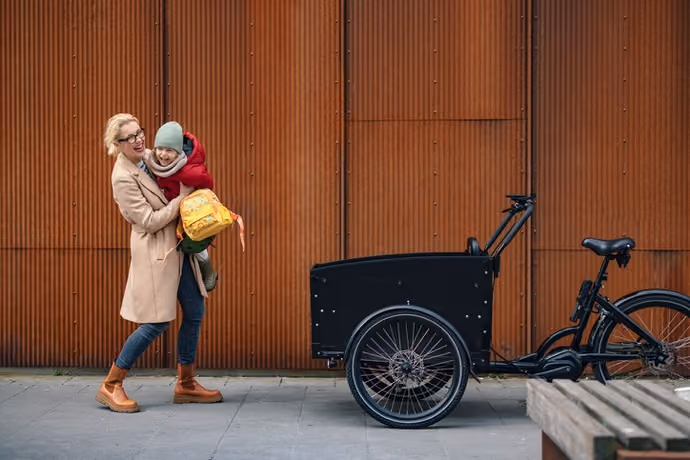 mother carrying child towards cargo bike