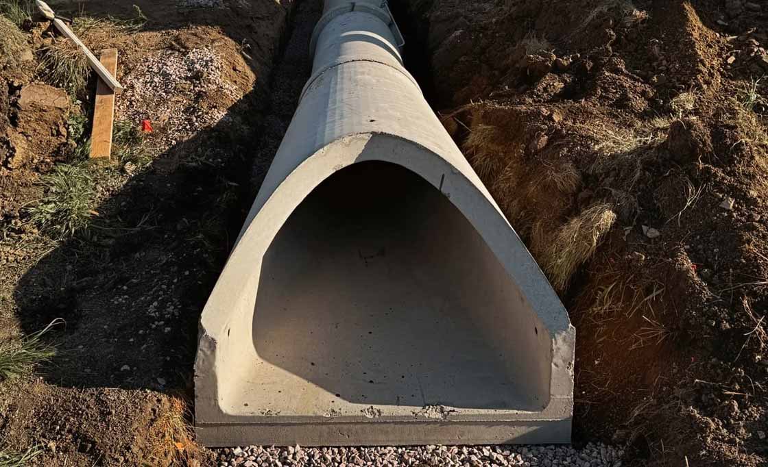 Large concrete drainage pipe installed in a trench with exposed soil and gravel around it.