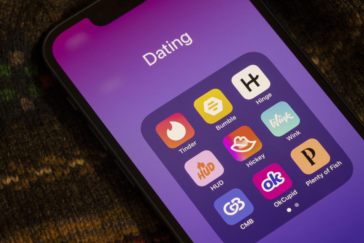 Smartphone-Display mit Ordner voller Dating-Apps wie Tinder, Bumble und Hinge auf violettem Hintergrund.