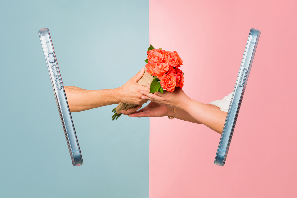 Strauß orangefarbener Rosen, der zwischen zwei aus Smartphones herausragenden Händen über blau-rosa geteiltem Hintergrund überreicht wird