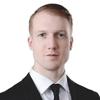 Portrait of a man with very short, ginger hair, wearing a black suit and tie with a white shirt.