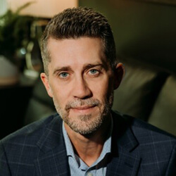 Smiling man wearing a dark navy sport jacket and light blue button-up shirt.
