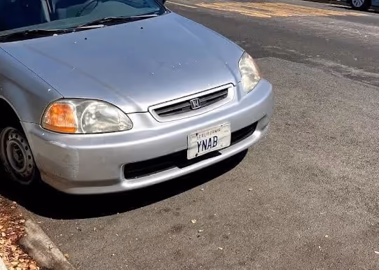 Front view of a silver Honda car parked on a street with a California license plate reading 'YNAB'.