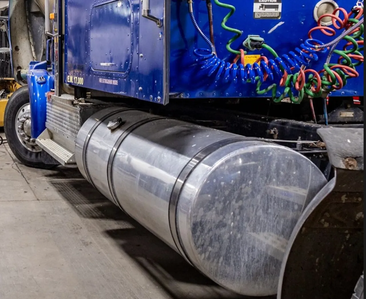 EGR & DPF repair on a semi-truck in a service bay with fuel tank, air lines, and cab side visible. Text: "CAUTION" and "EM 17,000".