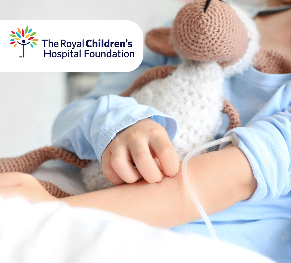 Crop of a child in a hospital bed, cuddling a soft lamb toy. In the corner of the image, the logo of The Royal Children's Hospital Foundation.