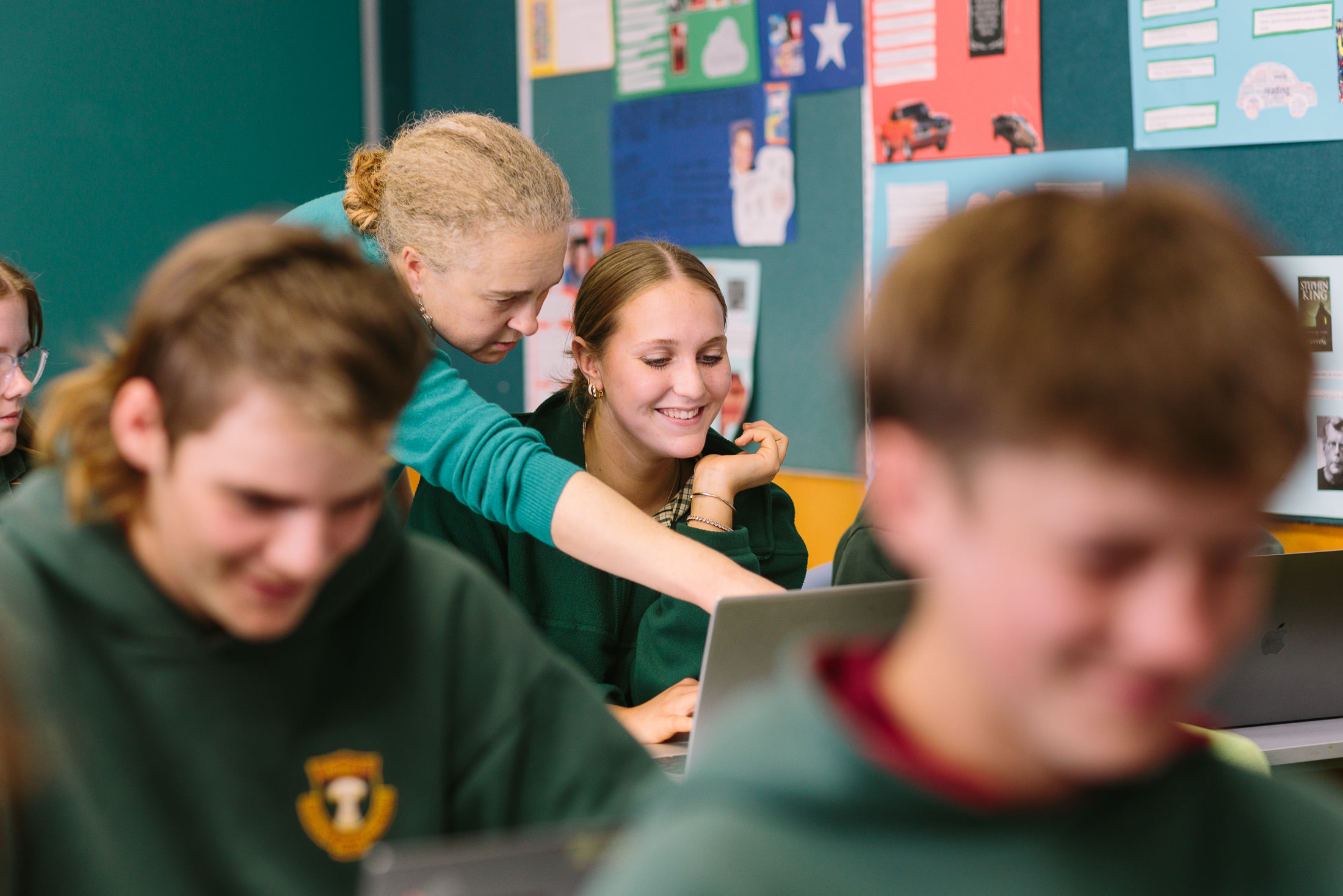 genuine, candid school marketing photography. Teacher helping student at her computer in classroom full of happy, hard working students. Palms Photography Adelaide commercial photographer 