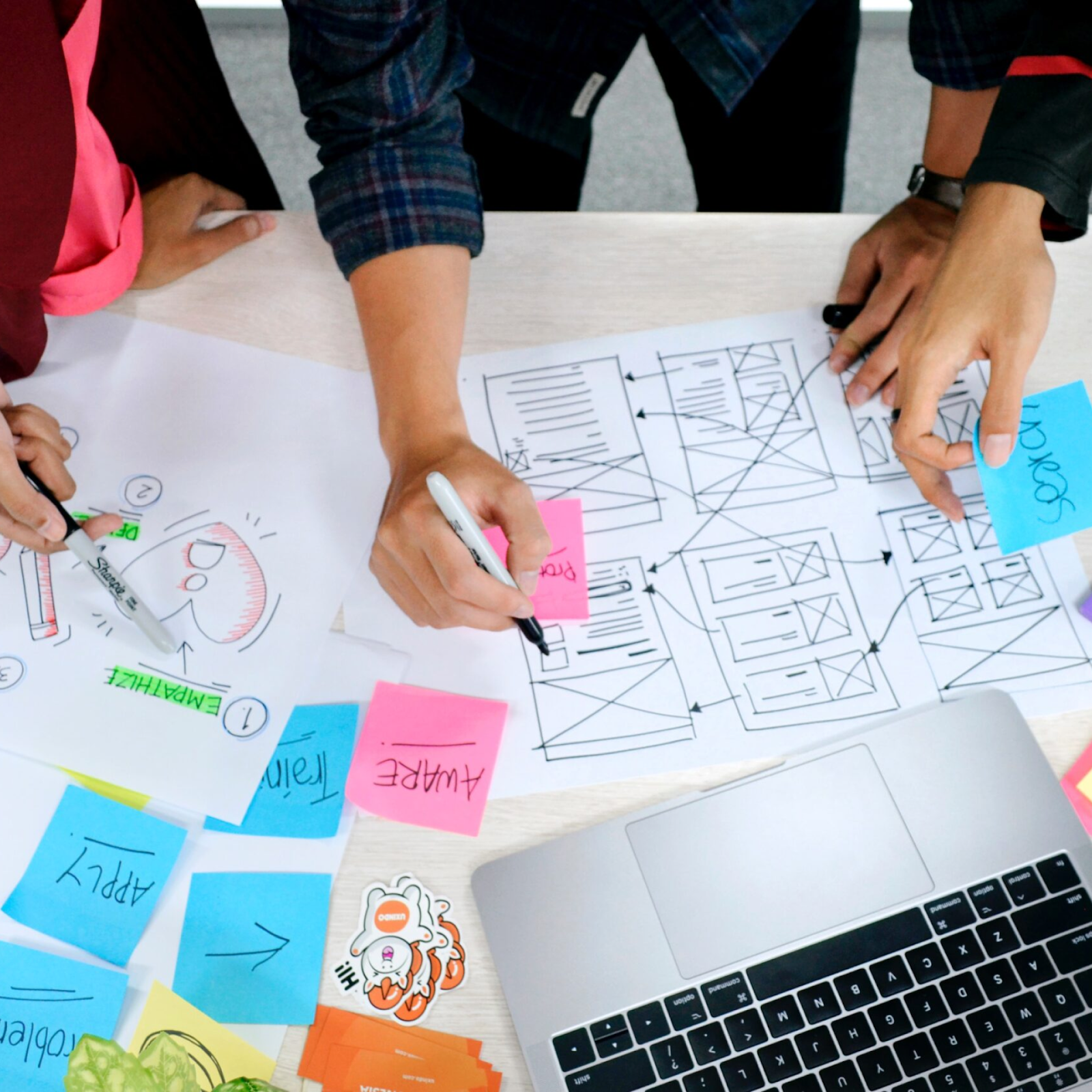 Team collaborating on app wireframes with sketches, sticky notes, and a laptop on the table.