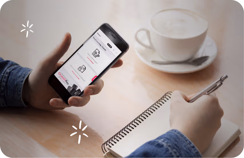 Image of a hand holding crunch software on a phone with one hand and writing with the other hand.