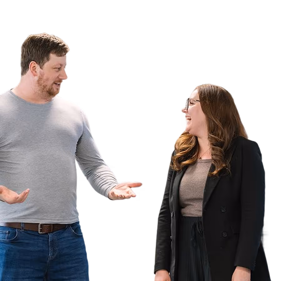 Man in gray shirt and jeans talking and gesturing with woman in black blazer and glasses.