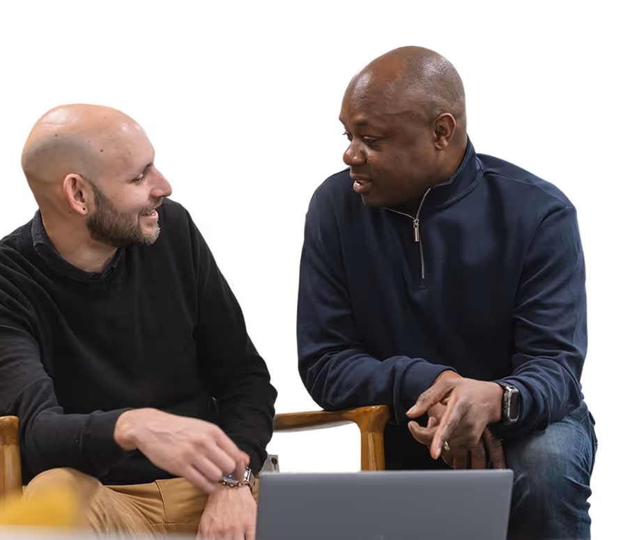 Two men sitting and conversing, one with a laptop in front of them.