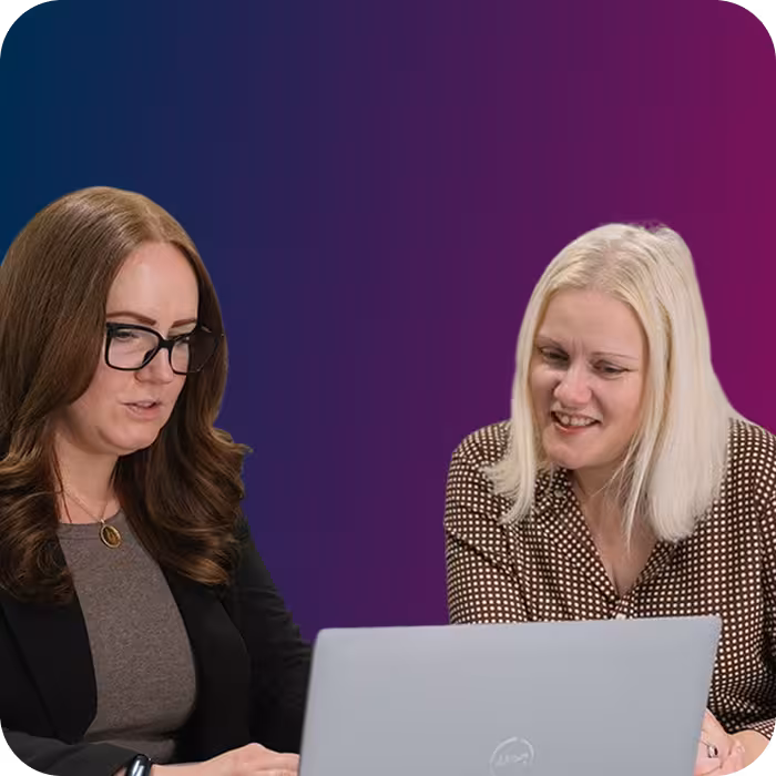 Two women looking at a laptop screen, one with glasses and brown hair, the other with blonde hair.