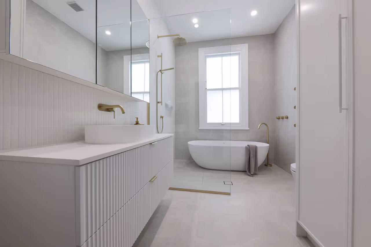 Modern bathroom with white freestanding tub, glass shower, brass fixtures, and a white vanity with vessel sink.