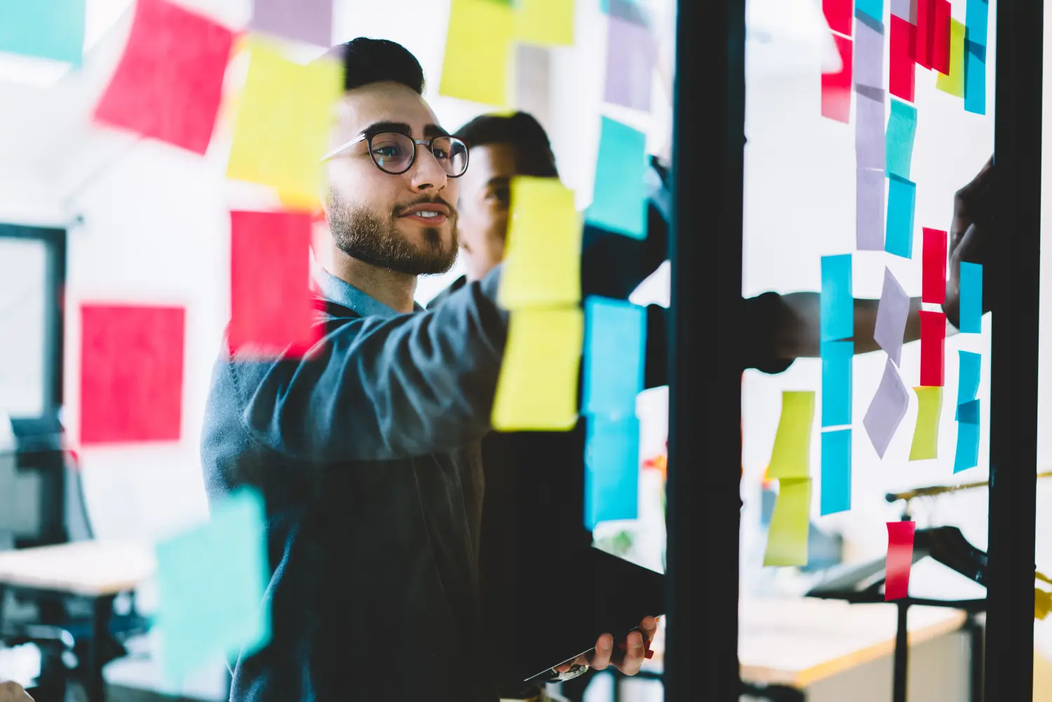 Vielfältiges Team aus qualifizierten jungen Menschen, die während des Zusammenarbeitsprozesses im Büro Fremdwörter mithilfe von bunten Aufklebern lernen, die auf eine Glaswand geklebt sind