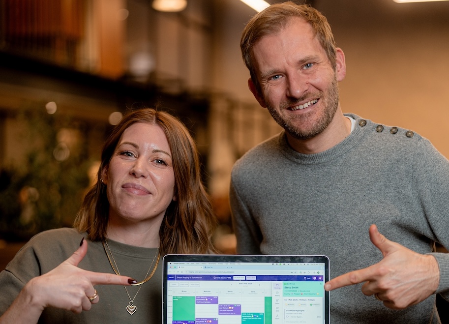 Two people smiling and pointing at a tablet that shows the Slick calendar