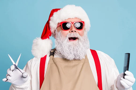 Santa in sunglasses and a stylist's apron, holding scissors and a comb