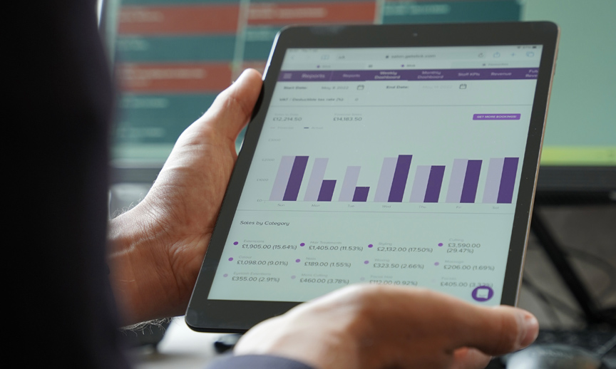 Hands holding a tablet that shows a Slick sales report with a bar chart