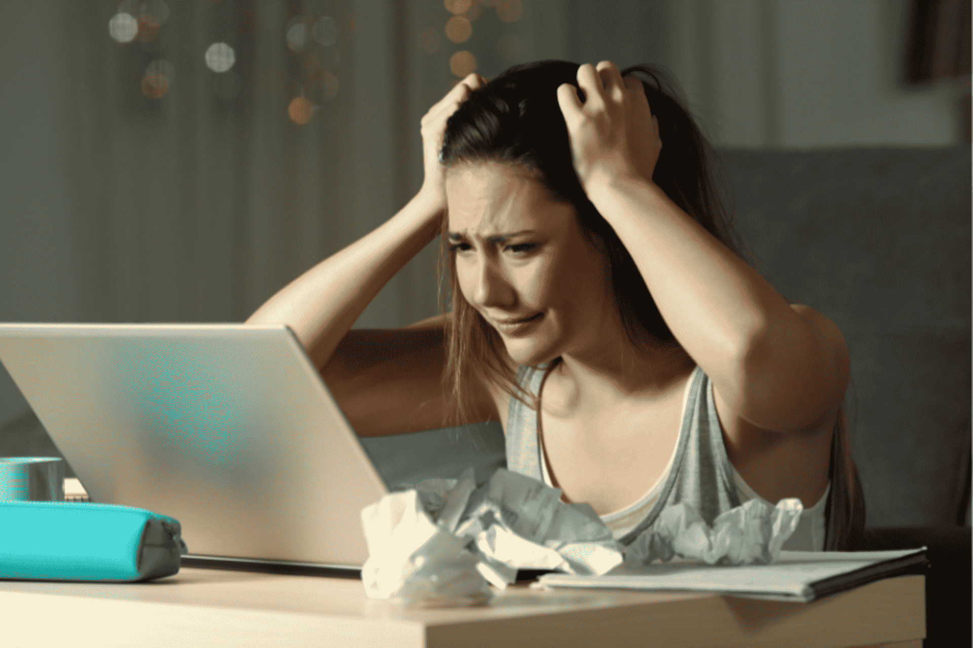 Stressed woman with her hands in her hair, sitting in front of a laptop