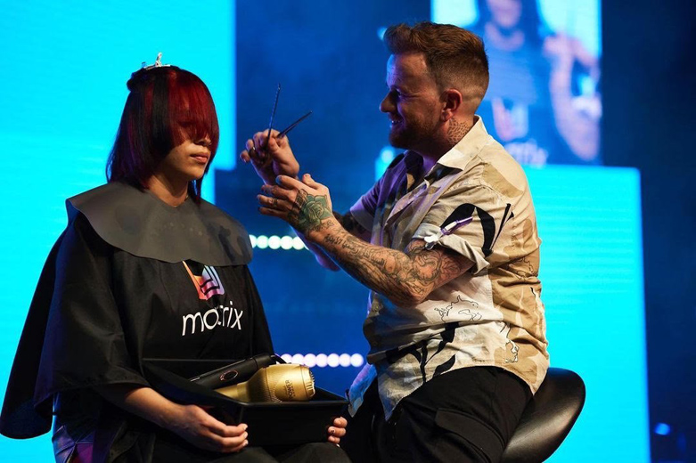 Hairdresser cutting a model's red hair on stage at a live event