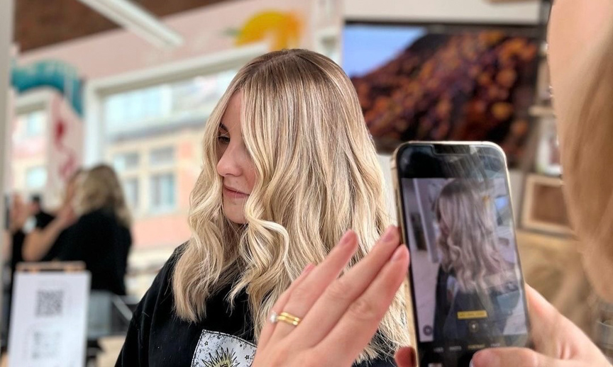 Stylist taking a photo of a client's finished blonde waves on a smartphone