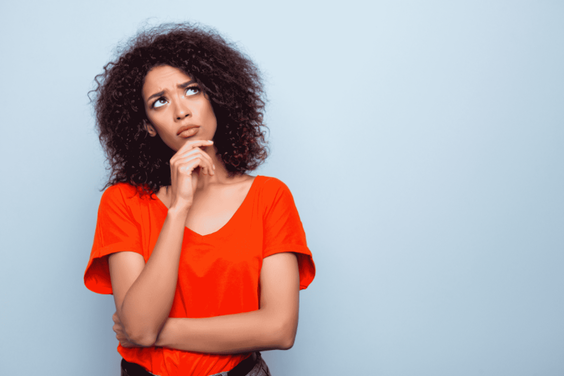 Woman in an orange T-shirt looking up thoughtfully, with her hand on her chin