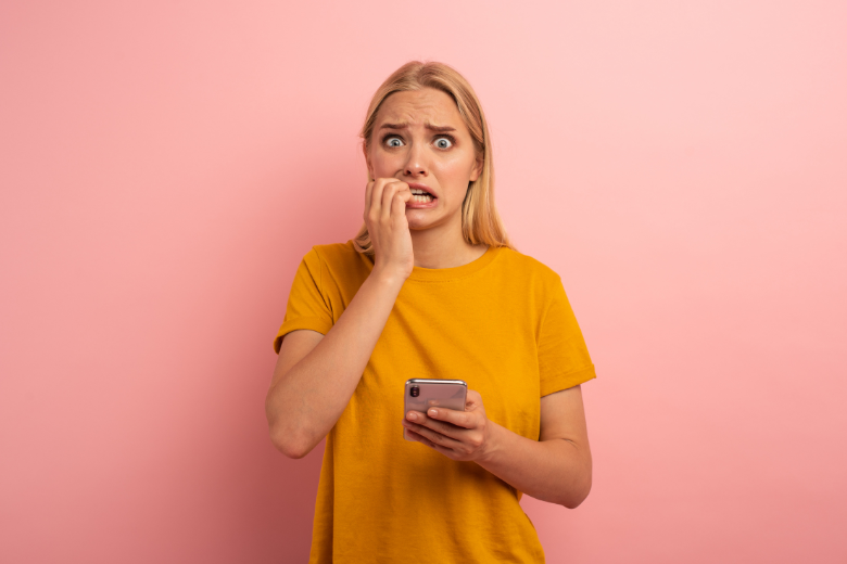 Woman looking anxious and biting her nails while she holds her phone