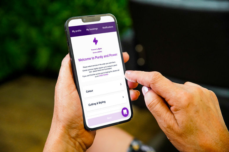 Hand holding a phone that shows a salon's Slick online booking page
