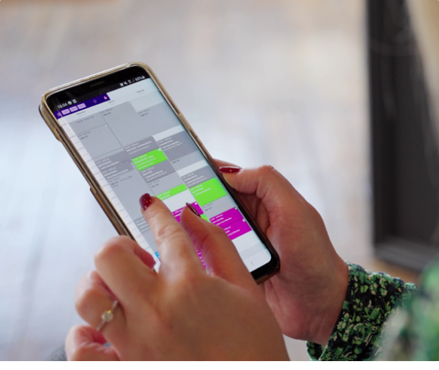 Hands holding a smartphone that shows a salon booking calendar