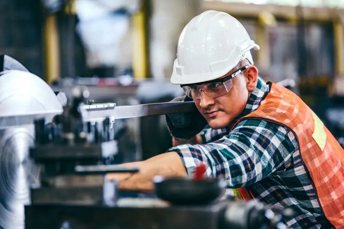 Man in manufacturing facility bending down and working with a saw.