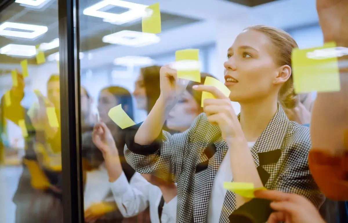 People placing sticky notes onto a glass wall.