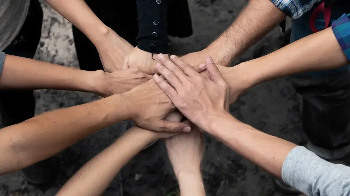 Hands stacked on top of each other with people standing in a circle.