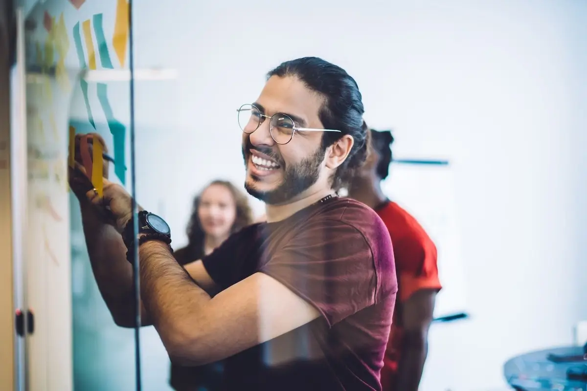 Man looking at camera while writing something on the wall in front of him.