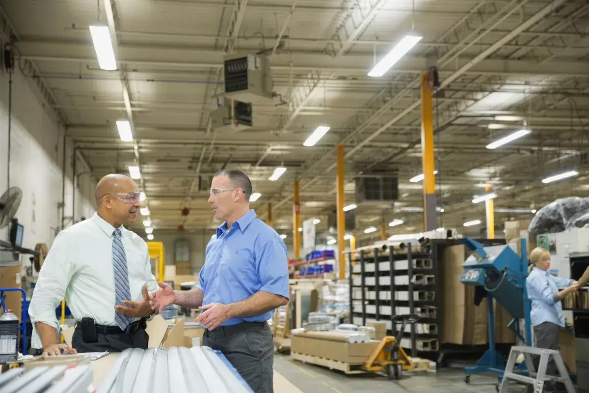 Two people having a conversation in the middle of a manufacturing facility.
