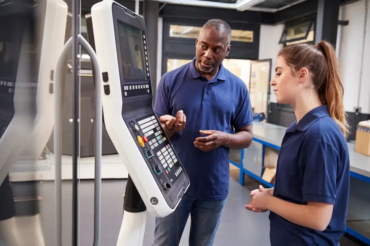 Two people in a manufacturing facility working on a machine.