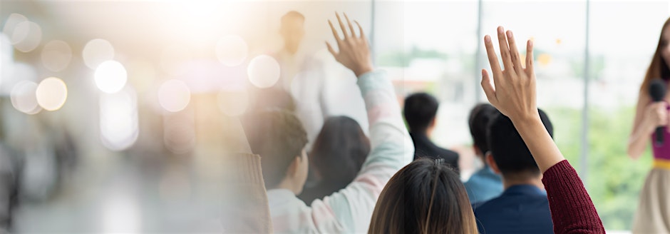 Room of people at a conference raising their hand.