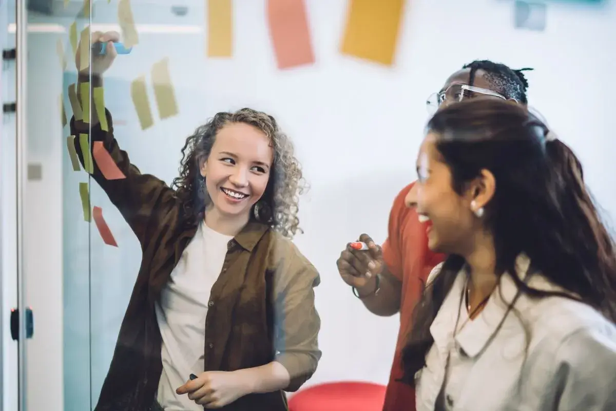 Three people looking at a wall with sticky notes on it and collaborating.