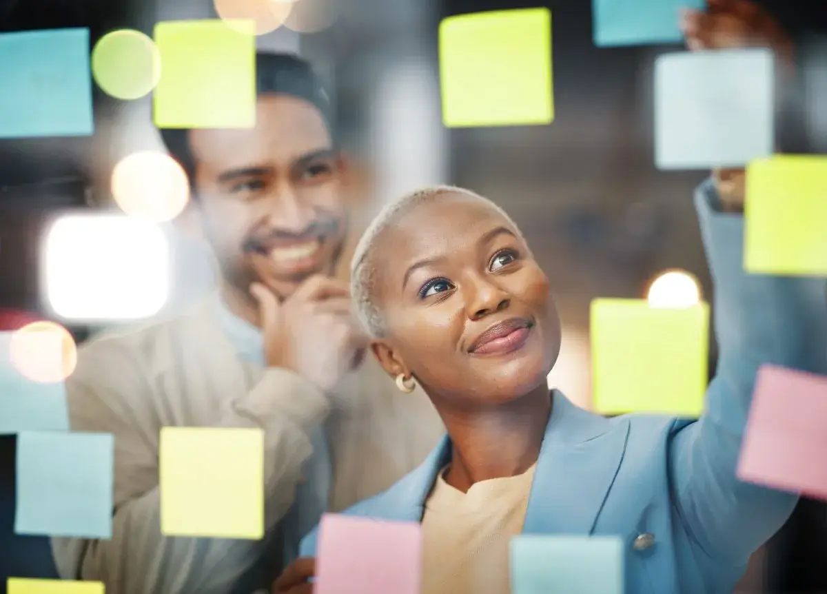 Close-up shot of two people looking at pink, yellow, bue, and green sticky notes on a wall.