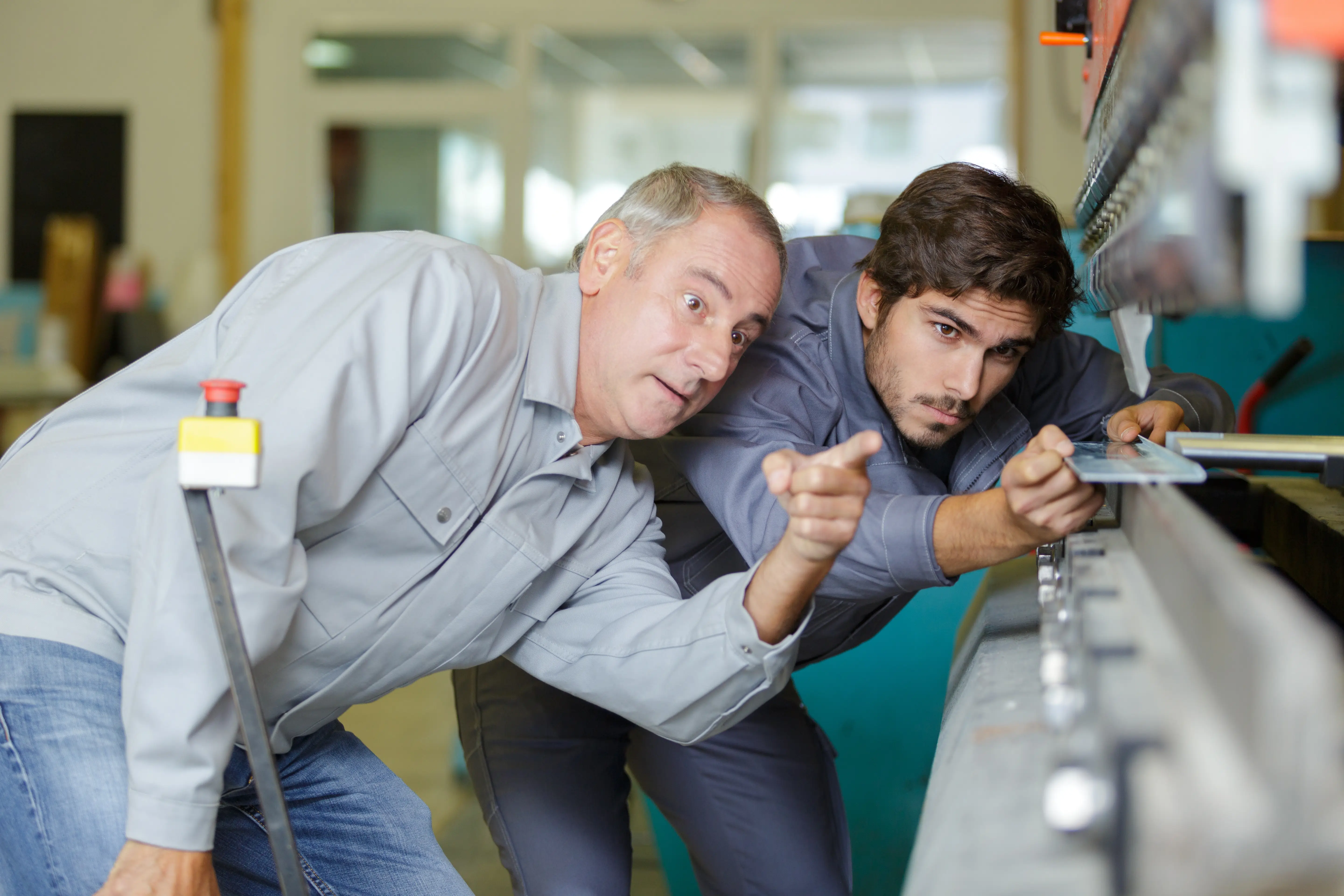 Two men looking at a specific object in a manufacturing facility while the one on the left points as the one on the right is adjusting the object.