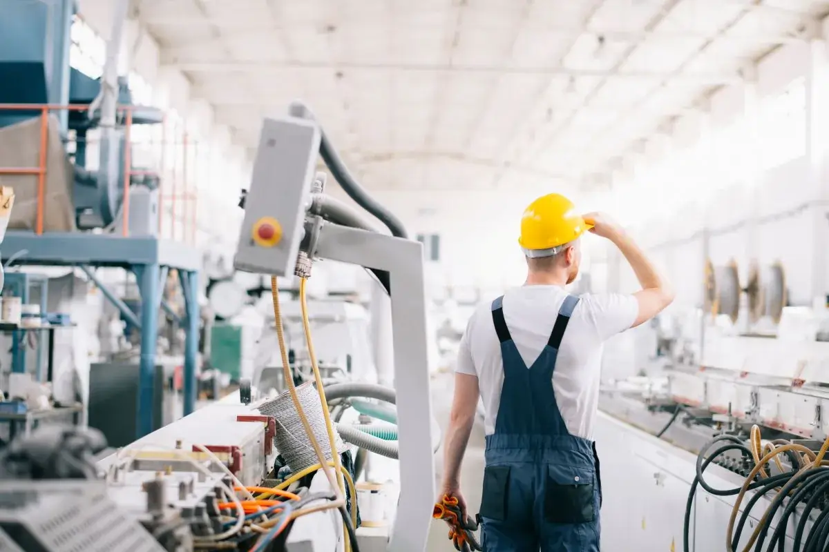 Person in manufacturing facility wearing an overall and a yellow hard hat.