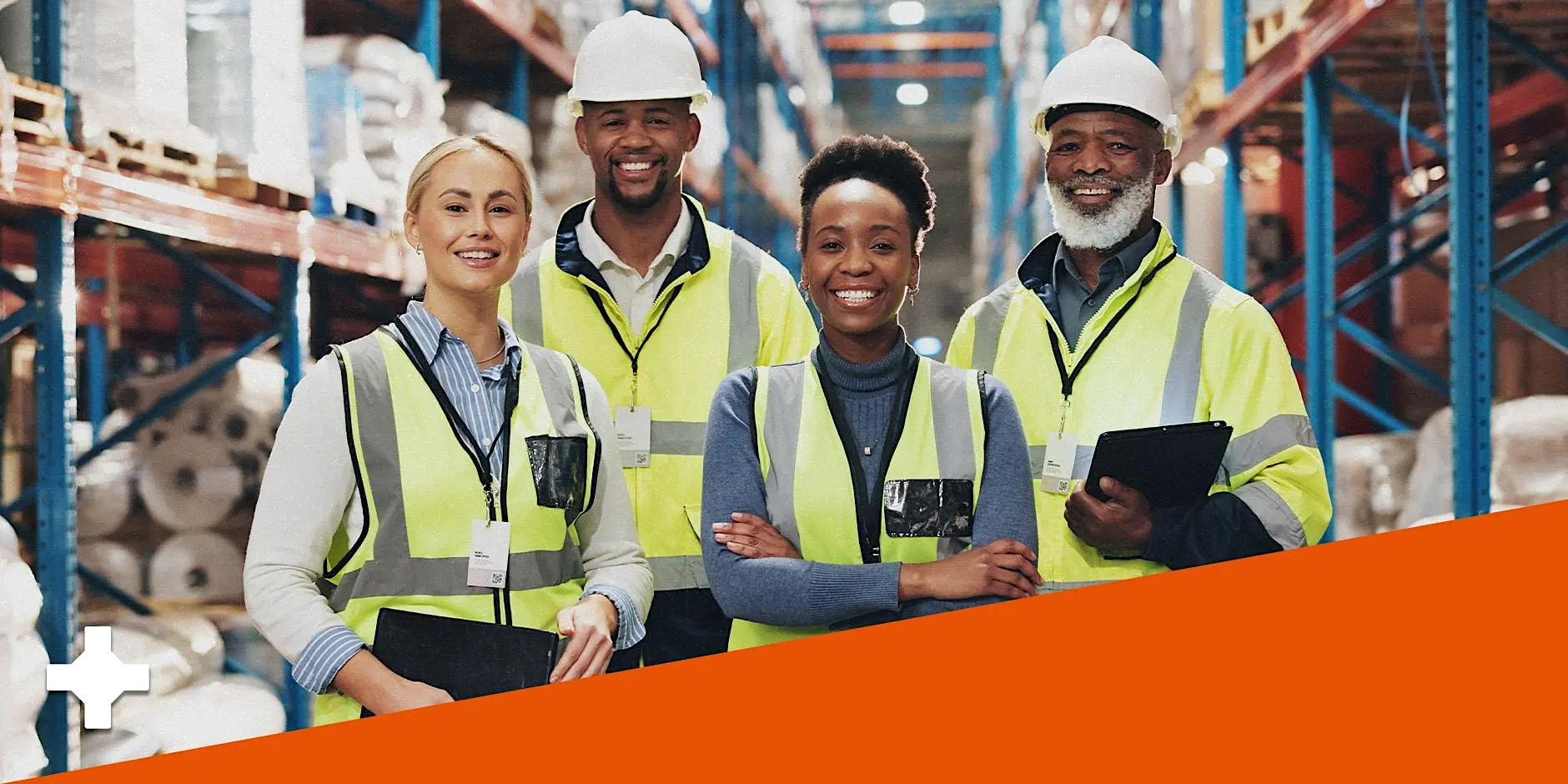 Two women and two men standing in a manufacturing facility wearing yellow and gray vests while looking at the camera and smiling.