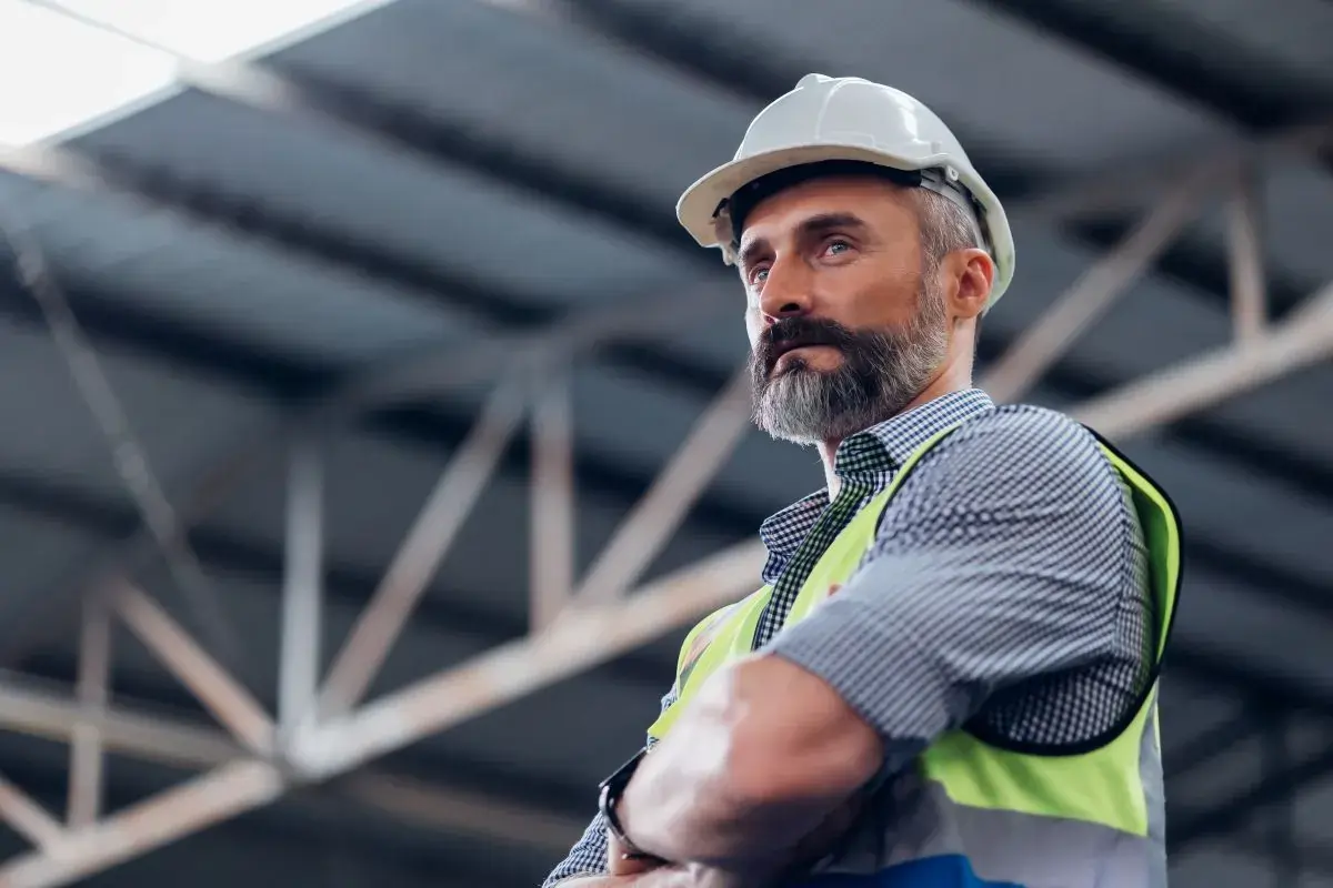 Man in a manufacturing facility with his arms crossed in manufacturing attire looking away from the camera.