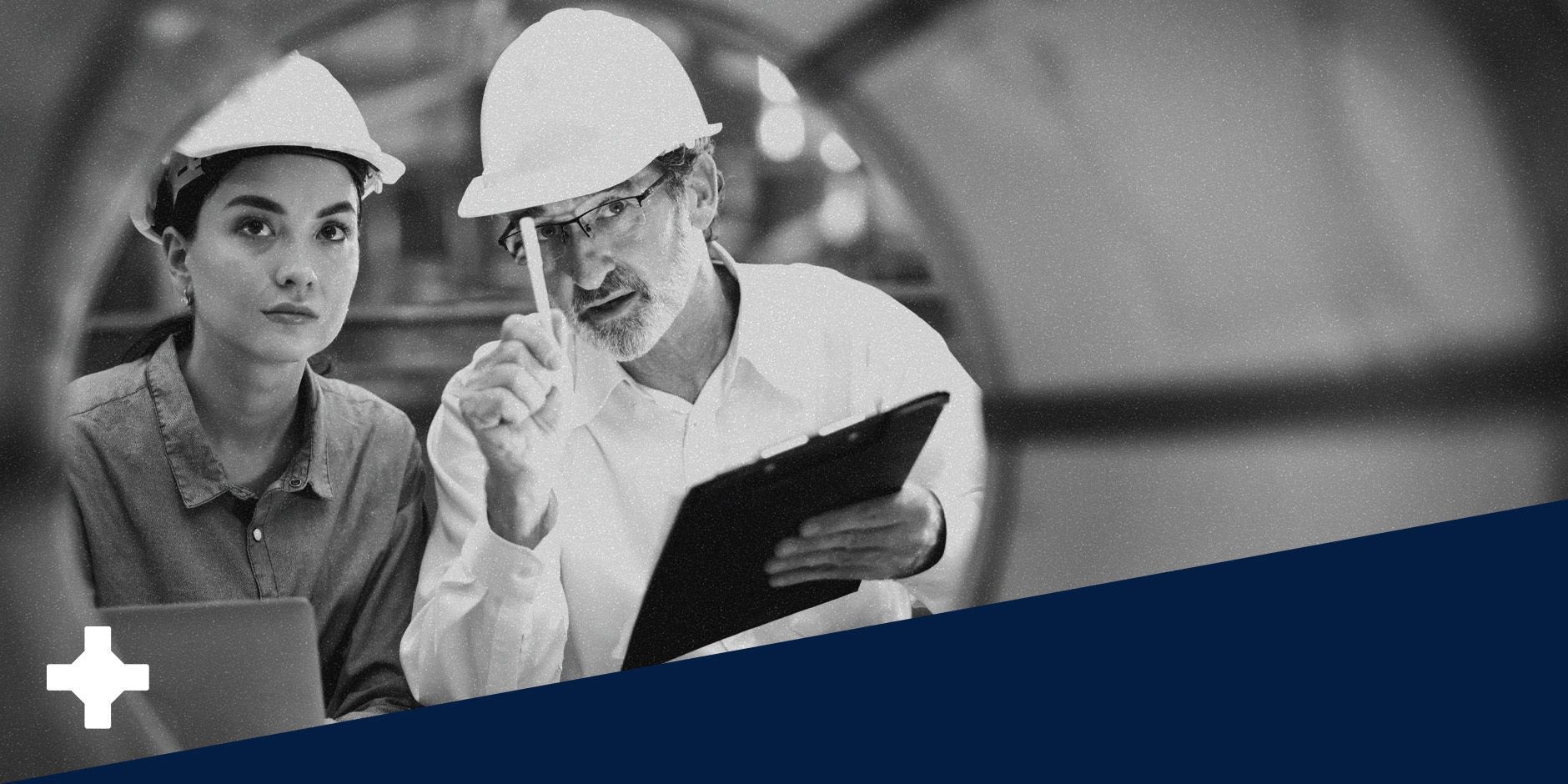 Two people in a manufacturing facility while the one on the right holds a tablet. The photo is black and white with a navy blue color at the bottom.