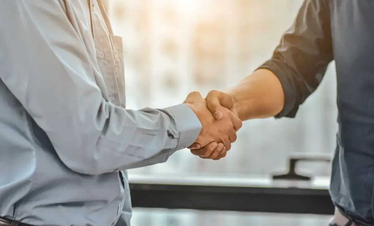 Two people shaking hands in an office with just the handshake being shown.