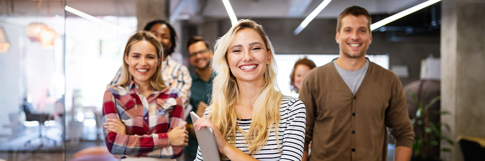 Young professionals standing in an office space and smiling.