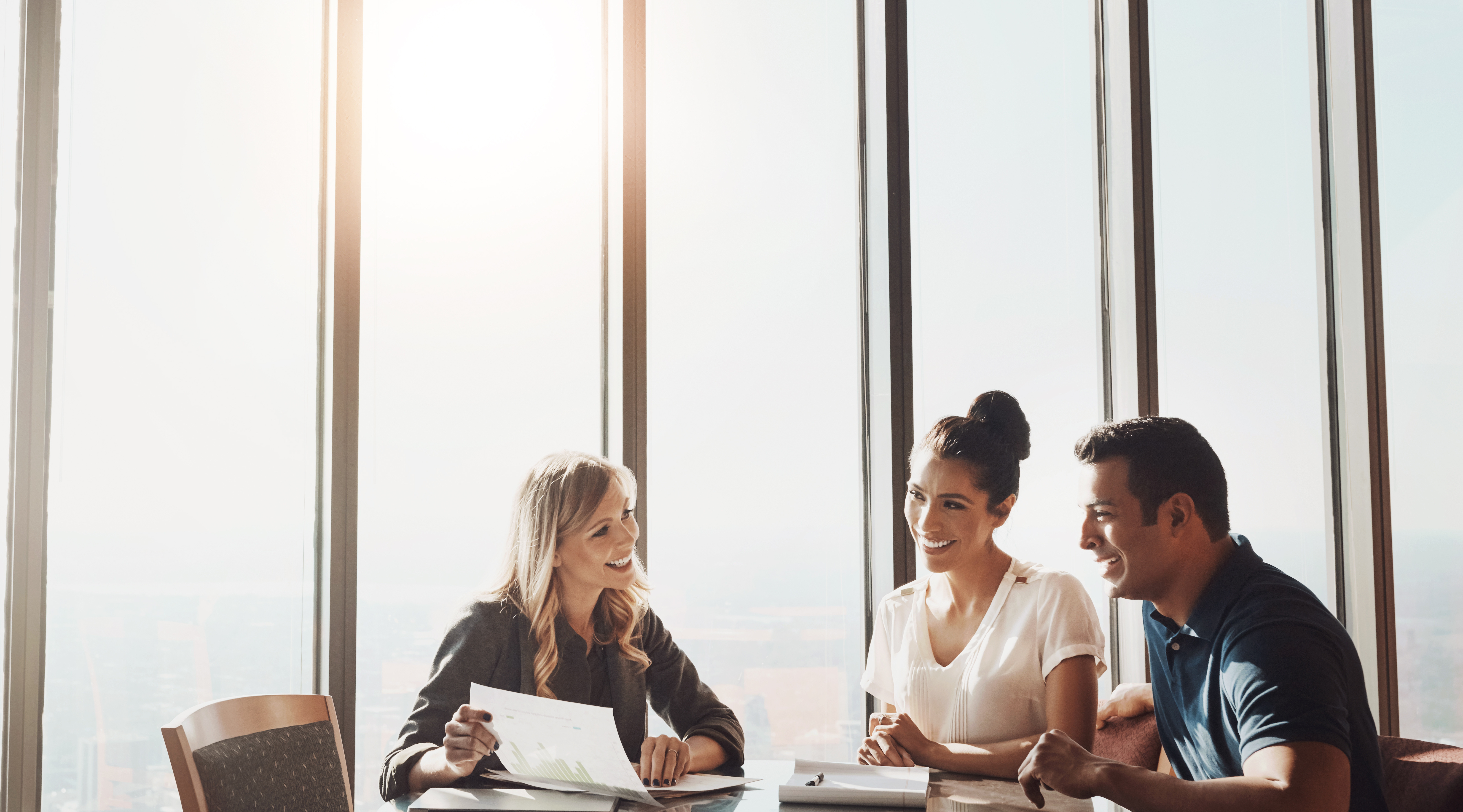 A financial advisor reviews papers with a couple in front of tall windows.