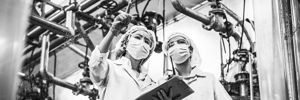 Five people wearing lab coats in a manufacturing facility while crossing their arms and looking at the camera.